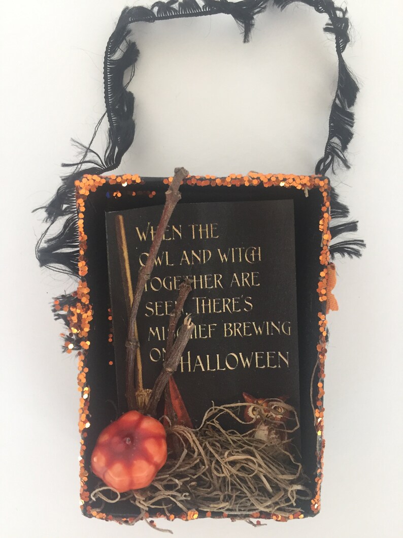 Pu&ograve; includere: Una scatola decorativa a tema Halloween con manico nero e bordo glitterato arancione. All'interno, una carta nera con testo dorato recita: "Quando il gufo e la strega si vedono insieme, c'&egrave; malizia in preparazione ad Halloween".