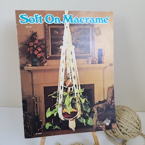 May include: A vintage macrame pattern book with a cover image of a white macrame plant hanger with a green plant inside. The book is titled "Soft On Macrame" and has the number HH-13 printed on the cover.