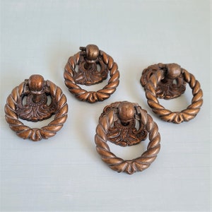 Peut inclure: Quatre tirettes de tiroir en bronze antique avec des motifs ornés. Chaque tirette a une forme de bague avec un élément central décoratif.