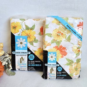 May include: Two packs of Penn-Prest Fashion Manor no-iron muslin bedding. The bedding features a floral print with yellow, orange, and green flowers on a white background. The packs include one sheet and two pillowcases. The text on the packs reads "Penn-Prest", "Fashion Manor", "No-Iron Muslin", "Never Needs Ironing", "50% Fortrel Polyester 50% Cotton", "One sheet double bed 81 x 104", and "2 pillow cases 42 x 36".