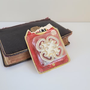 Peut inclure: Une garniture décorative blanche avec un motif doré, emballée dans une boîte rouge et blanche avec le texte "Instructions au verso".