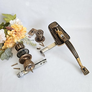 May include: A collection of vintage door hardware, featuring a handle, doorknobs, and a latch. The hardware is crafted from brass and bronze, with a dark finish and detailed patterns. The items are displayed on a white surface.