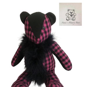 Puede incluir: Un oso de peluche de cuadros rosa y negro con un ribete de piel negra alrededor del cuello. El oso tiene ojos de botón negros y una nariz negra. El oso de peluche está sentado sobre un fondo blanco. El texto "Annie's Memory Bears" es visible en la esquina superior derecha de la imagen.