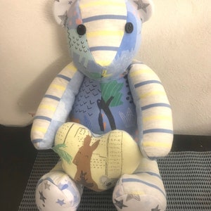 May include: A blue and white striped teddy bear with a heart-shaped patch on its chest. The heart patch features a kangaroo design. The bear has black button eyes and white stars on its ears and feet.