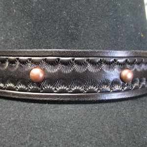 May include: A black felt cowboy hat with a black leather band and copper rivets. The band has a decorative embossed pattern.