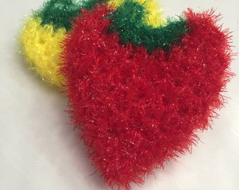 Puede incluir: Tres paños de cocina de crochet en forma de corazón en rojo, amarillo y verde. El paño de cocina rojo está en primer plano y los paños de cocina amarillo y verde están detrás.