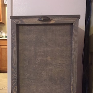 May include: A grey wooden bin with a hinged door and a metal handle. The bin has a simple design and is made from reclaimed wood.