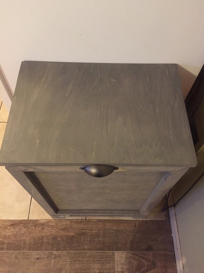 May include: A grey wooden cabinet with a single door and a black metal handle. The cabinet is sitting on a wood floor.