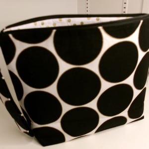 Könnte beinhalten: Schwarze und weiße Polka-Dot-Schminktasche mit Reißverschluss und silbernem Riemen.