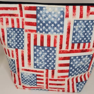 Könnte beinhalten: Eine rote, weiße und blaue Reißverschlusstasche mit einem abgenutzten Muster der amerikanischen Flagge. Die Tasche hat einen Reißverschluss und einen Stoffgriff.