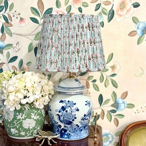 May include: A table lamp with a blue and white ceramic ginger jar base featuring bird and floral motifs, topped with a pleated light blue fabric lampshade decorated with a repeating pink and green floral pattern on a brass-toned metal fitting.