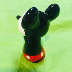 May include: A black and white ceramic figurine of Mickey Mouse. Mickey is wearing red shorts with white polka dots. He is standing on a green surface.