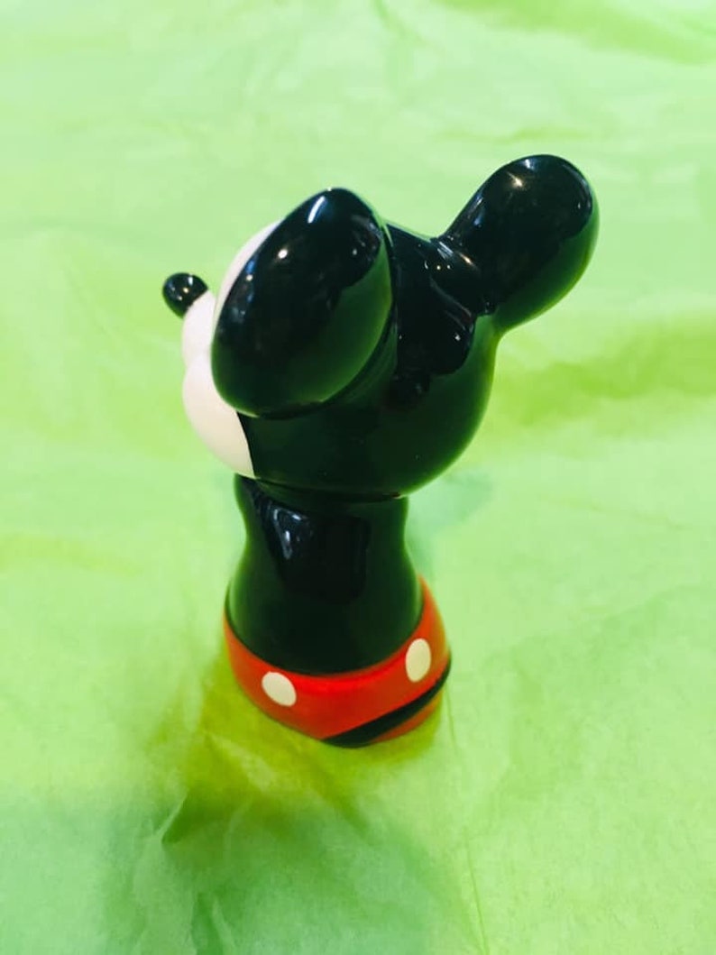 May include: A black and white ceramic figurine of Mickey Mouse. Mickey is wearing red shorts with white polka dots. He is standing on a green surface.