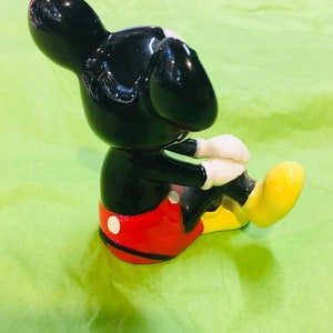 May include: A black ceramic figurine of Mickey Mouse sitting with his legs crossed. He is wearing red shorts with white polka dots and yellow shoes.