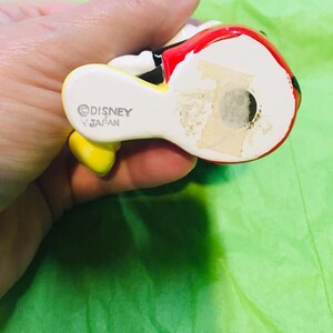 May include: A ceramic figurine of Mickey Mouse wearing a red and yellow outfit. The figurine is made in Japan and has the Disney copyright symbol on the bottom.