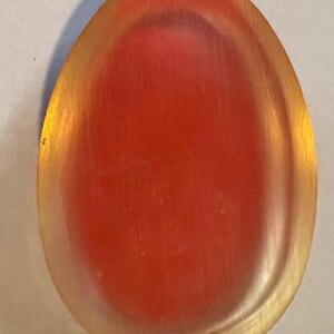 K&ouml;nnte beinhalten: Ein ovales Objekt mit einer glatten, durchscheinenden Oberfl&auml;che. Die Mitte weist einen tiefen, leuchtend roten Farbton auf, der in einen warmen, goldgelben Rand am &auml;u&szlig;eren Bereich &uuml;bergeht und einen Verlaufseffekt auf dem St&uuml;ck erzeugt.