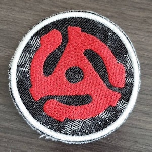 May include: A red vinyl record logo embroidered on a black and white fabric patch with a white border.