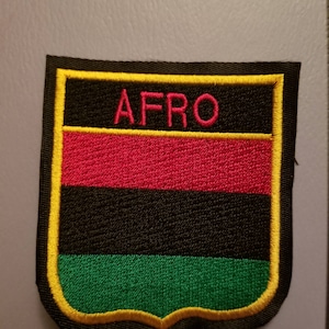 May include: Embroidered patch with the word "AFRO" in pink letters. The patch features a black background with horizontal stripes of red, black, and green. The patch is outlined in yellow and black.