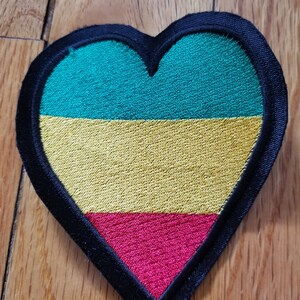 May include: A heart-shaped patch with a black border and three horizontal stripes in green, yellow, and red.