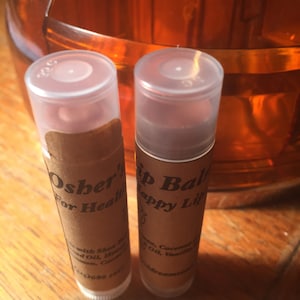 May include: Two brown tubes of lip balm with white caps. The tube on the left says "Osher's For Healthy Lips" and the tube on the right says "Lip Balm Happy Lips".