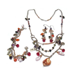Peut inclure: Un collier multi-rangs avec une variété de perles colorées, notamment roses, rouges, oranges et vertes. Le collier présente également une grosse perle en cuivre de forme irrégulière. Le collier est assorti de boucles d'oreilles.