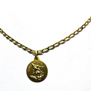 Puede incluir: Un collar dorado con un colgante redondo con la inscripci&oacute;n "SAINT MICHEL" y una imagen de un &aacute;ngel. La cadena es de dise&ntilde;o de eslabones. El colgante tiene un aspecto envejecido.