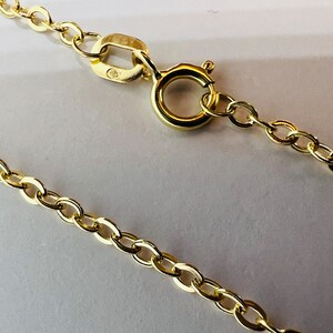 May include: Close-up of a gold-colored necklace chain with an oval link design. The chain is secured with a spring ring clasp. The jewelry is displayed on a white surface.