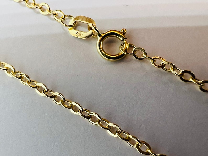 May include: Close-up of a gold-colored necklace chain with an oval link design. The chain is secured with a spring ring clasp. The jewelry is displayed on a white surface.