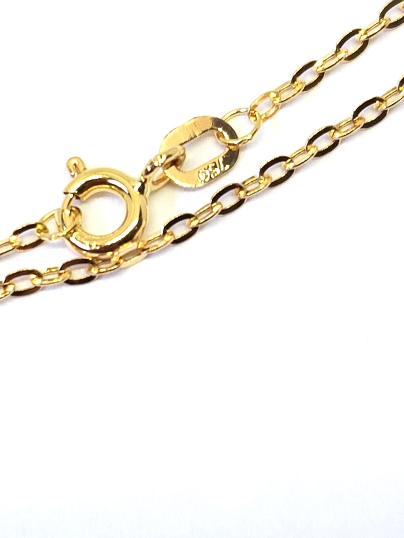 May include: Close-up of a delicate gold necklace with an oval link chain. The necklace features a lobster clasp and a small tag with the marking "750". The chain is displayed against a white background.
