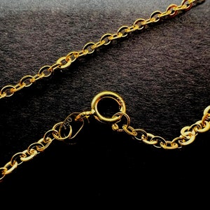 May include: Close-up of a gold necklace with an oval link chain. The necklace has a lobster clasp closure and a small tag with the number "750" stamped on it. The chain is displayed against a dark background.