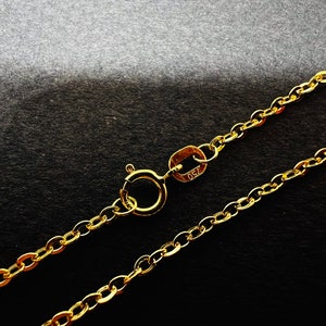 May include: A gold-colored necklace with a delicate chain and a spring ring clasp. The necklace is displayed against a dark background. The clasp is marked with the number "750".