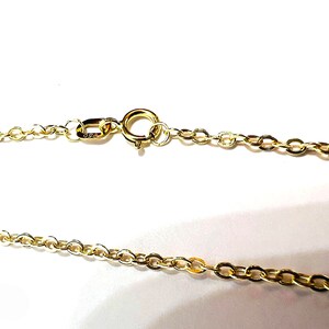 May include: Close-up of a gold-colored necklace chain with a spring ring clasp. The chain is made of small, oval-shaped links. The clasp is attached to the chain with a small jump ring. The necklace is on a white background.