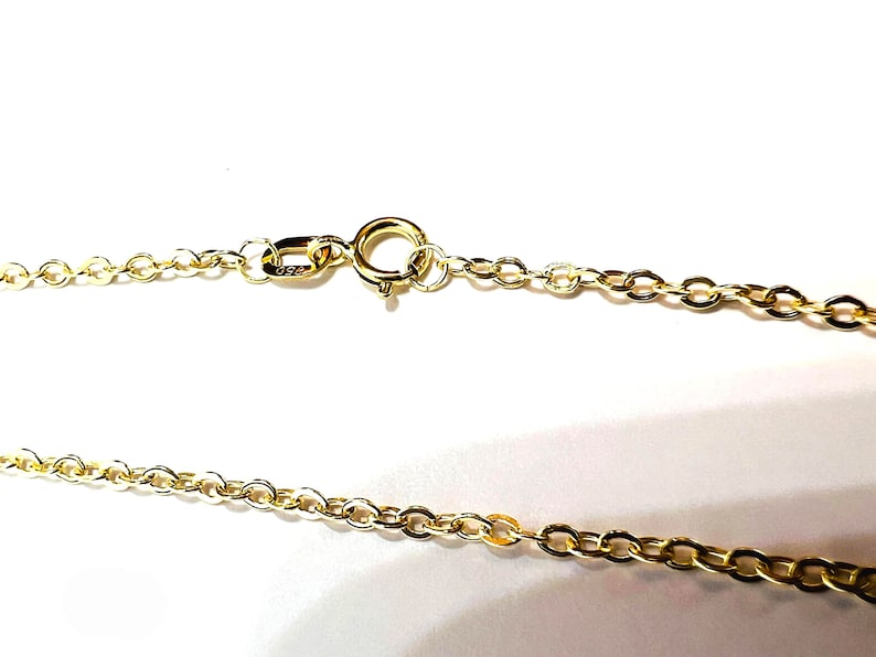 May include: Close-up of a gold-colored necklace chain with a spring ring clasp. The chain is made of small, oval-shaped links. The clasp is attached to the chain with a small jump ring. The necklace is on a white background.