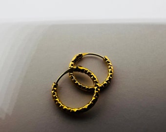 Può includere: Un paio di orecchini a cerchio dorati con un design testurizzato a forma di diamante.
