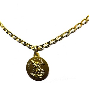 Puede incluir: Un collar dorado con un colgante que representa a San Miguel. El colgante redondo tiene las palabras "SAINT MICHEL" alrededor de la imagen. La cadena es una cadena figaro dorada.