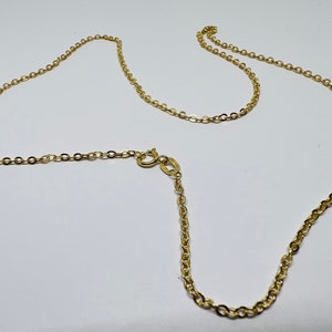 May include: A delicate gold-colored chain necklace with a lobster clasp. The chain is made of small, interconnected oval links. The necklace is displayed on a white surface.