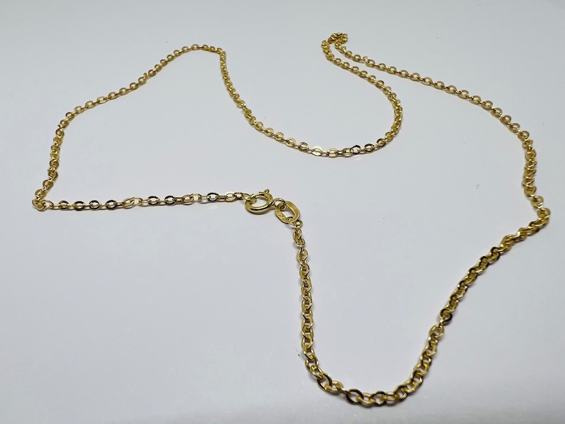 May include: A delicate gold-colored chain necklace with a lobster clasp. The chain is made of small, interconnected oval links. The necklace is displayed on a white surface.