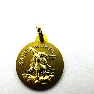 Puede incluir: Colgante de San Miguel dorado con el texto "SAINT MICHEL" y una representaci&oacute;n de San Miguel. El colgante tiene un lazo en la parte superior con el n&uacute;mero "750" grabado. El colgante es redondo y tiene un acabado mate.