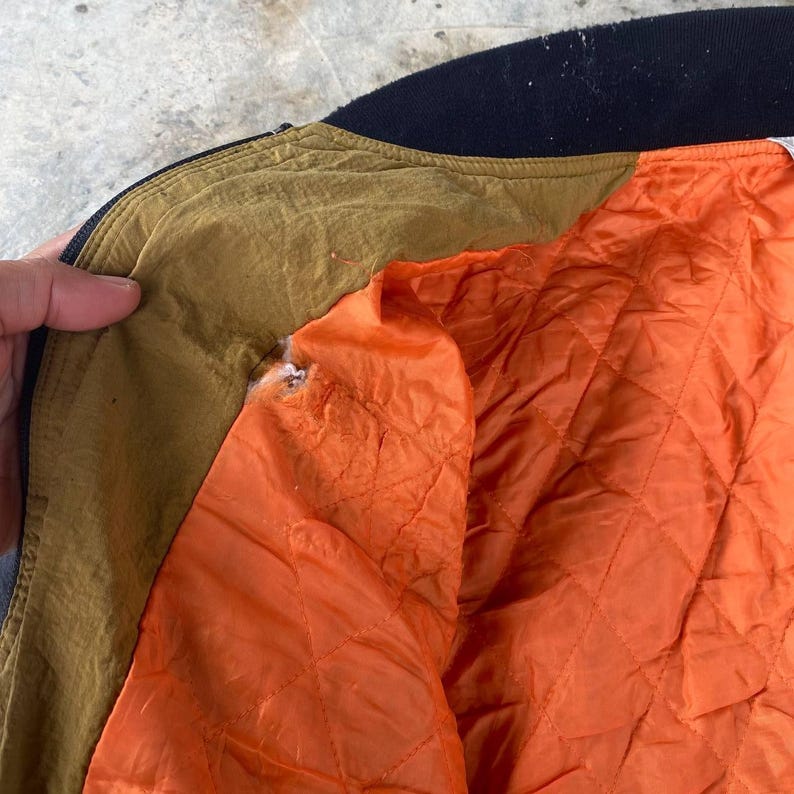May include: Close-up of the inside of a brown and black bomber jacket. The lining is a bright orange quilted fabric.