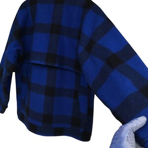 Puede incluir: Chaqueta a cuadros azul y negro. La chaqueta presenta un patr&oacute;n de cuadros cl&aacute;sico en tonos azules y negros. Tiene un bolsillo en la espalda y cierre de botones. La manga es visible en la imagen.