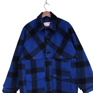 Puede incluir: Una chaqueta a cuadros azul y negro con cuello y cuatro bolsillos delanteros. La chaqueta est&aacute; colgada de una percha de madera. La chaqueta tiene cierre de botones y est&aacute; hecha de un material grueso y c&aacute;lido.