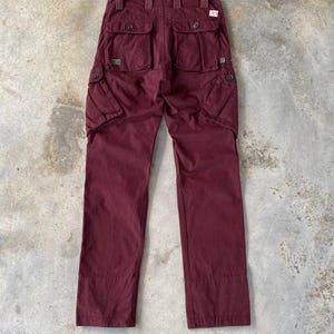 Puede incluir: Un pantalón cargo de color burdeos con múltiples bolsillos y cierre de botón.