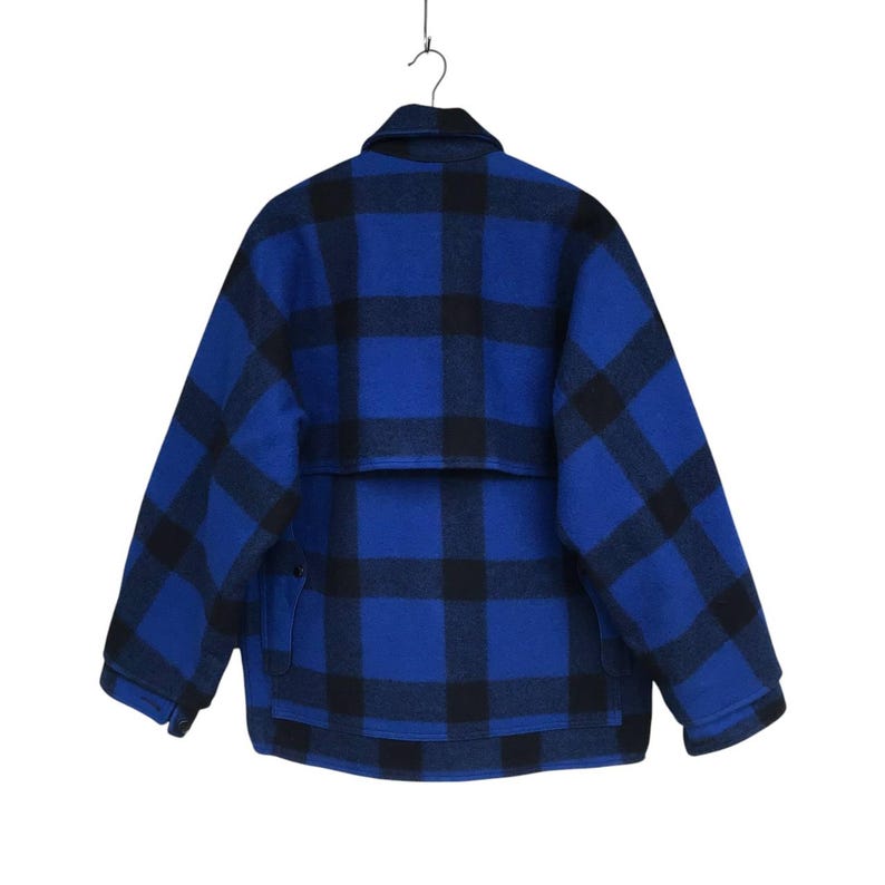 Puede incluir: Una chaqueta a cuadros azul y negro colgada de una percha met&aacute;lica. La chaqueta tiene cuello, dos bolsillos delanteros y una solapa trasera. La chaqueta est&aacute; hecha de un material grueso y c&aacute;lido.