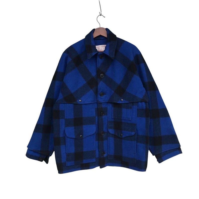 Puede incluir: Chaqueta a cuadros azules y negros con cierre de botones, dos bolsillos en el pecho y dos bolsillos inferiores. La chaqueta est&aacute; colgada de una percha de madera.