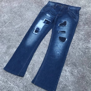 May include: A pair of blue denim jeans with distressed details and patches. The jeans have several rips and tears, and the patches are sewn on in a patchwork style.