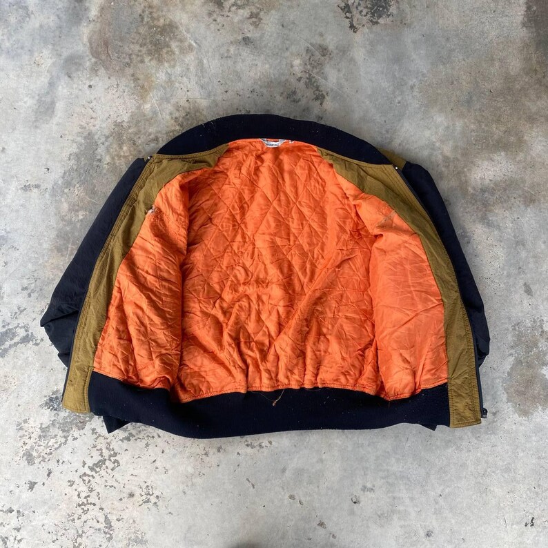 May include: A brown and black bomber jacket with an orange quilted lining. The jacket is unzipped and laid flat, showing the inside lining.