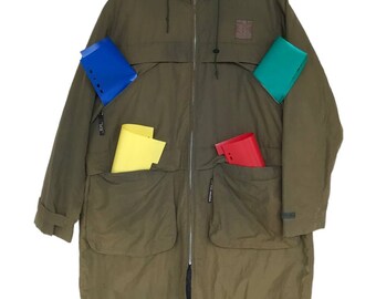 Könnte beinhalten: Eine lange, olivgrüne Kapuzenjacke mit mehreren Taschen. Die Jacke hat einen Reißverschluss und eine Kapuze mit Kordelzug. Die Jacke hängt an einem Kleiderbügel.