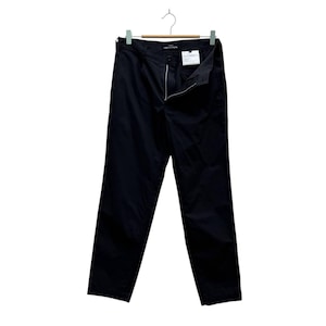 Puede incluir: Pantalones negros colgados de una percha de madera. Los pantalones tienen cremallera y cierre de botón, con una pequeña etiqueta adjunta. La tela parece ser un material ligero. Los pantalones son de color negro liso.