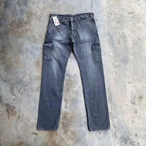 Puede incluir: Pantalones cargo vaqueros grises con dos bolsillos laterales y una etiqueta. Los pantalones tienen un diseño de pierna recta y cierre de botón y cremallera. El denim tiene un aspecto descolorido.