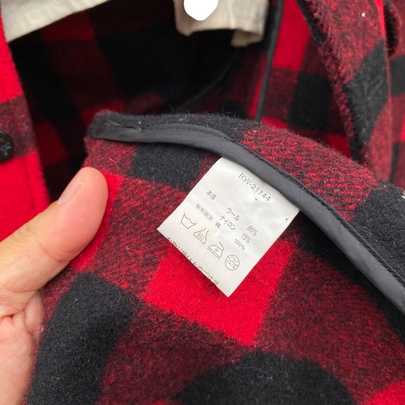 May include: A red and black plaid flannel shirt with a label that reads "RW-21744" and lists the fabric composition as 85% wool and 15% nylon. The label also states that the separate fabric portion is 100% cotton.